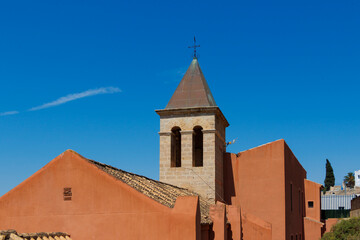 Historical building with a pointed bell tower in Alicante, featuring vibrant orange walls and a...