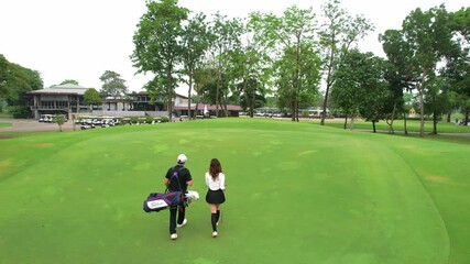 Drone view of male and female golfers walk across lush green fairway. - Powered by Adobe