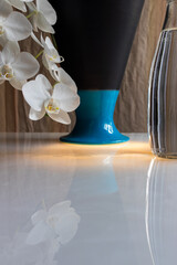 still life with white orchid, blue vase and glass bottle with water on marble
