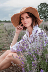 Portrait of a young sexy beautiful woman in straw hat enjoying the scent of flowers, nature and relaxation while sitting  in a lavender field.