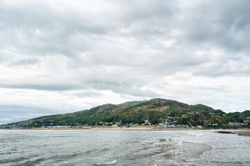 A scenic view of a green hillside peninsula stretching into the sea, with a small coastal village...