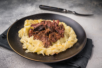 German Braised Beef Cheek, Slow cooked meat with smashed potatoes on a plate. grey background. top view