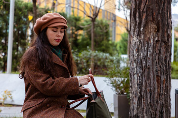 Stylish Caucasian woman resting on a park bench with her purse during a calm city walk. Relaxation,...