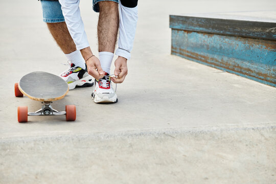 Young man ties shoelaces while preparing to skateboard at park during bright sunny afternoon