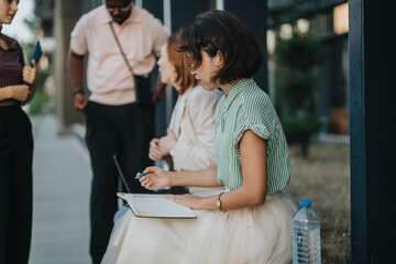 A group of young business people engage in a casual outdoor meeting. They are brainstorming and...