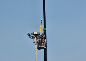 The crane lifting personnel baskets with two worker for sportlight lamp installation at highway lighting pole on blue sky background.