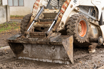 A skid steer is prepping the ground at a construction site nestled in nature, signaling ongoing...