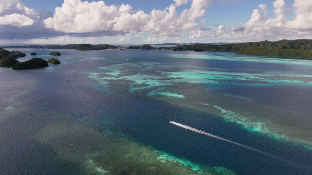 Elegant drone orbiting shot circling and revealing the vivid aqua ocean and green-covered terrain in Palau. boat in the water. Orbiting wide drone shot