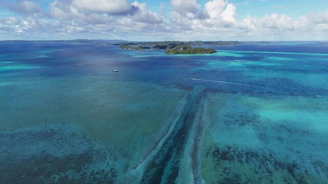 Captivating drone footage circling and revealing the vibrant blue ocean and scenic islands of Palau. Wide shot of boats in the water in the distance