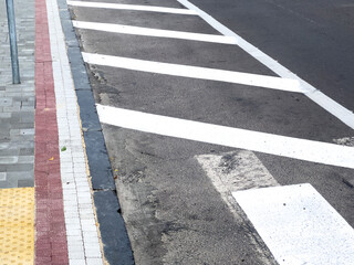 A clearly marked pedestrian crossing is visible alongside a textured sidewalk and road surface under bright sunlight in an urban area