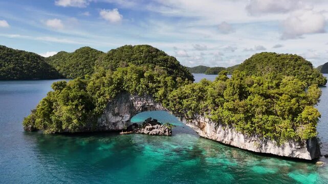 Drone flyover gliding around the crystal blue waters and islands in Palau, hovering beside an exposed rock face and overhang on an island. Cinematic aerial drone shot.