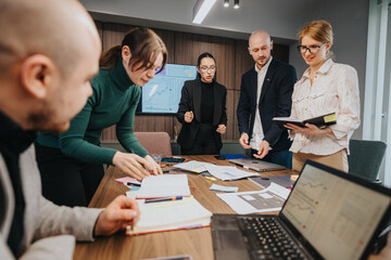 A cooperative team of employees working together in a modern office environment. They are brainstorming ideas with charts and notebooks visible, emphasizing teamwork, planning, and productivity.