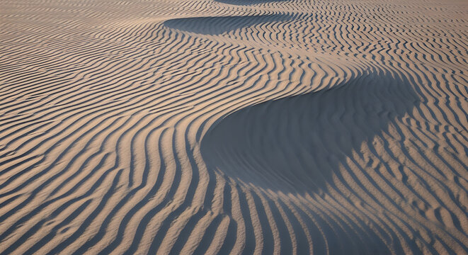 Aerial view of undulating sand dunes with visible wind patterns and shadows at sunset