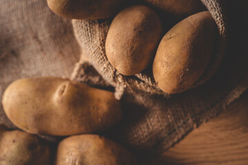 Fresh raw potatoes in a rustic burlap sack on a wooden surface. Organic vegetables displayed in a...