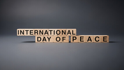 A minimalist photograph of wooden letter blocks spelling out the word "  International day of peace" arranged in a straight line on a dark gray background. 
