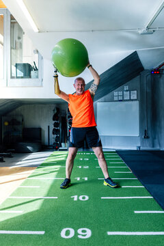 Athlete with prosthetic arm exercising with ball in modern gym