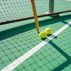 Two Tennis Balls by the Net Post on a Sunlit Court