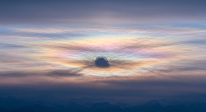 Stunning iridescent cloud, a rare nacreous cloud, with vibrant rainbow colors glowing like an aura. Ethereal atmospheric optical phenomenon (irisation) over a distant mountain range