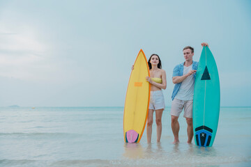 Happy young couple with surfboards enjoying a tropical beach holiday by the turquoise sea on a paradise island. capturing the lifestyle of happy people on a relaxing holiday by the ocean. baech.