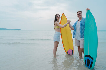 Happy young couple with surfboards enjoying a tropical beach holiday by the turquoise sea on a paradise island. capturing the lifestyle of happy people on a relaxing holiday by the ocean. baech.