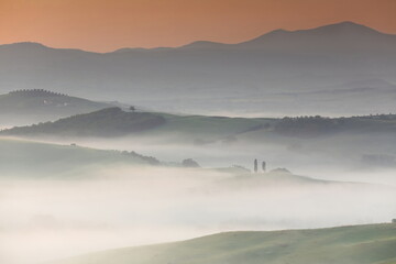 Colorful sky of a very foggy sunrise over Val d'Orcia Valley and its podere -farmsteads- among rolling hills. San Quirico d'Orcia-Tuscany-Italy-095