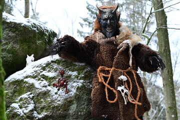 Teufelfigur im Winterwald. Mann mit geschnitzter Holzmaske mit Hörnern und teuflischem Grinsen...