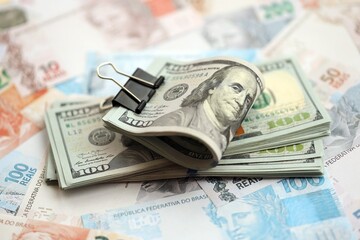 Bunch of US dollar bills lies on big amount of Brazilian reais banknotes close up