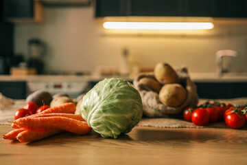 Fresh cabbage, carrots, and tomatoes arranged on a wooden kitchen table with a rustic background and warm lighting. Healthy homegrown vegetables