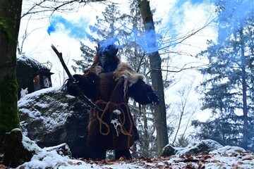 Teufelfigur im Winterwald. Mann mit geschnitzter Holzmaske mit Hörnern und teuflischem Grinsen...