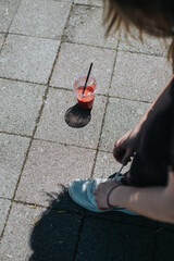 Colorful drink on pavement with focused individual tying shoe, highlighting outdoor and relaxation...