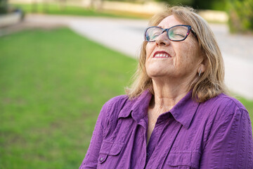 Senior woman breathing deeply, sitting peacefully amid sunlit greenery, embracing calm outdoor...