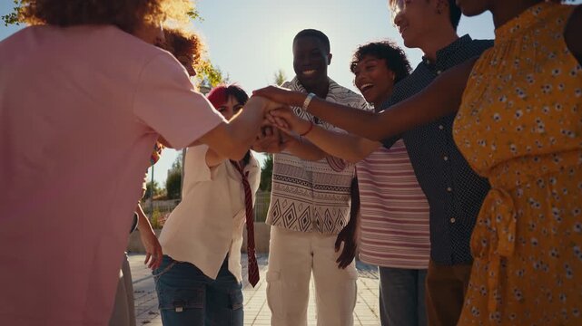 Multi-ethnic group of friends joining hands in a circle outdoors, symbolizing unity and teamwork, then raising arms in celebration of shared achievement