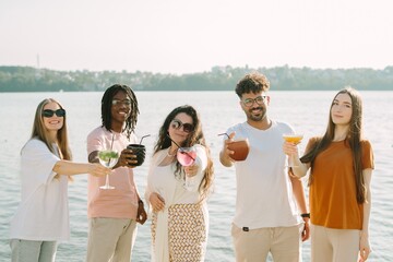Friends toasting cocktails by the lake on sunny day