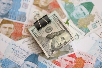 Roll of US dollar bills lies on big amount of Pakistan rupees banknotes close up