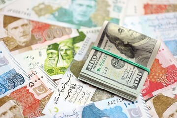 Stack of US dollar bills lies on big amount of Pakistan rupees banknotes close up