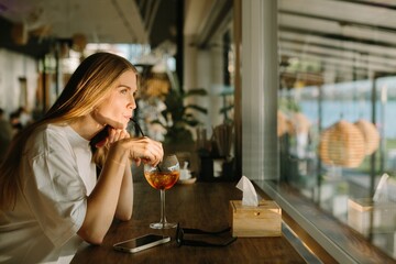Young woman enjoying a drink at a cafe, looking pensively through the window