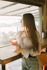 Young woman enjoying a refreshing drink at a cafe, gazing out the window