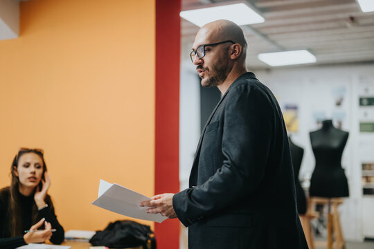 A teacher interacts with high school students in a creative classroom setting, emphasizing design concepts and effective communication. The image captures learning, engagement, and educational