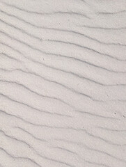 Top-down view of a natural sand texture background. Gentle wind-swept ripples create a serene and abstract wavy pattern.
