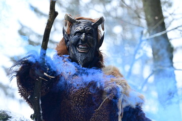 Teufelfigur im Winterwald. Mann mit geschnitzter Holzmaske mit Hörnern und teuflischem Grinsen...