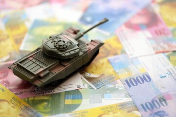 Swiss franc banknotes and toy tank. The current francs money bills and tank lies on table