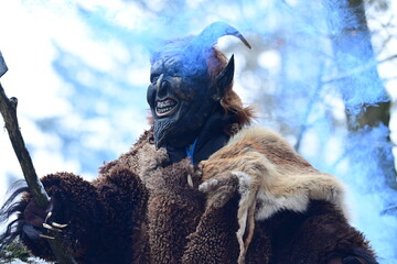 Teufelfigur im Winterwald. Mann mit geschnitzter Holzmaske mit Hörnern und teuflischem Grinsen...