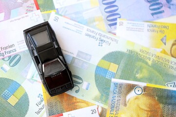 Swiss franc banknotes and toy car. The current francs money bills and black car lies on table