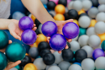 Hands Holding Purple Balls in Vibrant Ball Pit