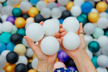 Hands Holding White Balls in a Colorful Ball Pit