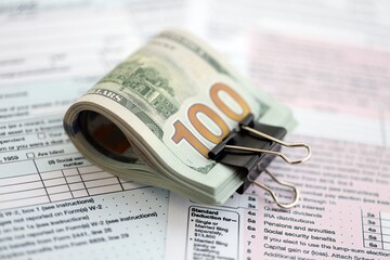 Big amount of United States USD dollar bills banknotes on table with 1040 tax return form