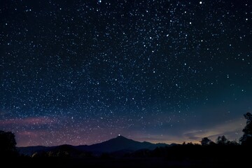 Fototapeta premium Night scene showing a starlit sky, mountain silhouette, and treeline below