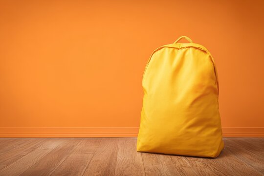 Bright yellow empty school backpack on orange background with wooden floor, clean minimalist design showcasing fabric quality for advertising or product display