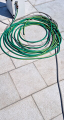 A green water hose coiled on a paved pier, with part of a boat utility pedestal visible in the...