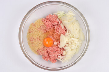 Aclear bowl with a mixture of raw ground meat, chopped onion, rice, and a single egg in the center, ready for preparation